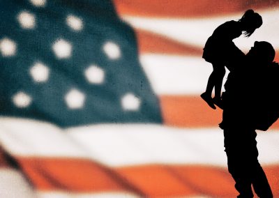 silhouette of soldier picking up child with American flag in the background